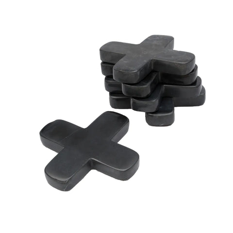 A stack of six black rubber cross-shaped objects, reminiscent of a stylish table setting accessory, with one additional cross lying flat in the foreground like a marble pan coaster.