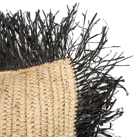 Close-up of a woven mat with beige fibers and a fringe of black, thin, jagged strands. The texture contrasts between the smooth surface and rough fringe, adding a boho touch reminiscent of a Raffia handwoven cushion in a villa-style home.