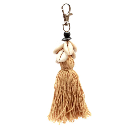 Discover the Boho luxury keychain with a gold clasp, adorned with decorative cowrie seashells and a cotton tassel of brown yarn elegantly hanging below.