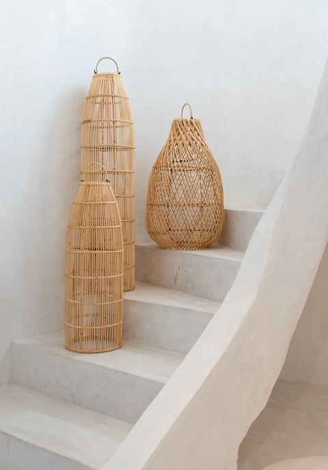 Three handwoven rattan baskets of varying heights are placed on white cement steps against a plain wall. Exuding rustic charm, the baskets are arranged in ascending order from the bottom step, adding an earthy elegance to their simple backdrop.