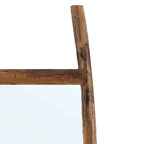 Close-up of a rustic wooden frame mirror crafted from reclaimed teak wood. The wood showcases a natural, weathered texture with visible knots and grain patterns, giving it a sturdy and handcrafted appearance. The bottom left corner of the mirror surface is partially visible.