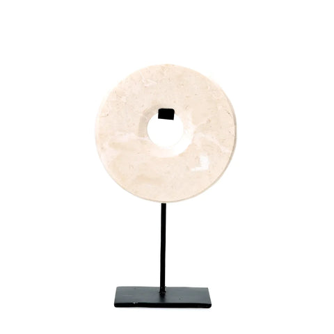 A Marble Disc sculpture featuring a central hole, mounted on a slender black stand and base, enhances any home interior. The decorative display boasts a textured, off-white stone surface against a plain white background.