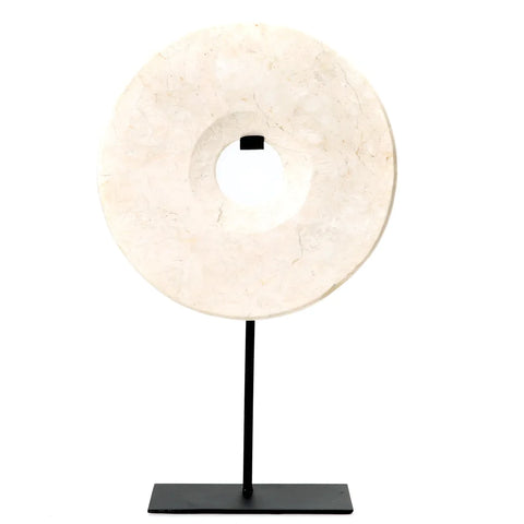 A chic touch to any space, the round beige marble disc with a central hole is elegantly mounted on a sleek black metal stand, perfect for a decorative display against a white background.