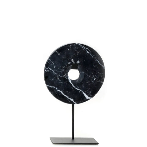 A decorative black marble disc with white veins, featuring a central circular hole, is mounted on a minimalist black metal stand. Perfect for enhancing your home interior, this elegant piece serves as a striking decorative display against a plain white background.