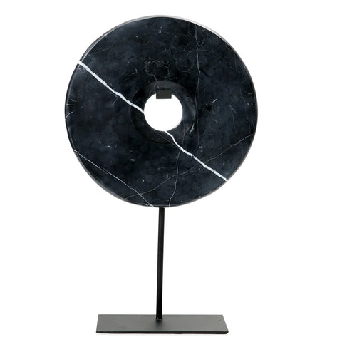 A large, round Marble Disc, with white veining and mounted on a simple black metal stand, complements any home interior. This striking decorative display features a noticeable crack running diagonally through the disc's central hole.