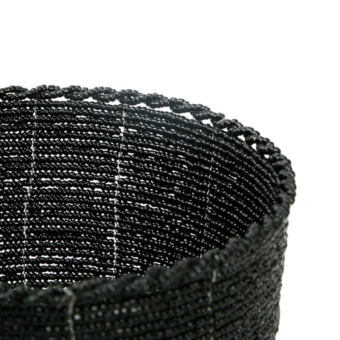 Close-up of a handmade beaded basket crafted from small black beads, intricately woven into a cylindrical shape. The texture and pattern of the beadwork are prominently visible, adding a touch of boho chic decorative flair. The background is plain white.