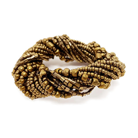 A twisted, brass-colored bracelet made of small, metallic beads and tiny square tiles, intricately woven together, resembling the elegance of gold beaded napkin rings that elevate any table setting.