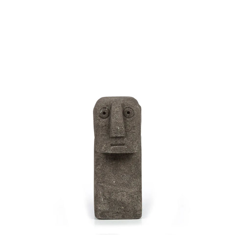 A small, dark Sumba Stone sculpture of a human face with simplified features, such as round eyes and a rectangular nose, hand carved from sandstone and set against a plain white background.