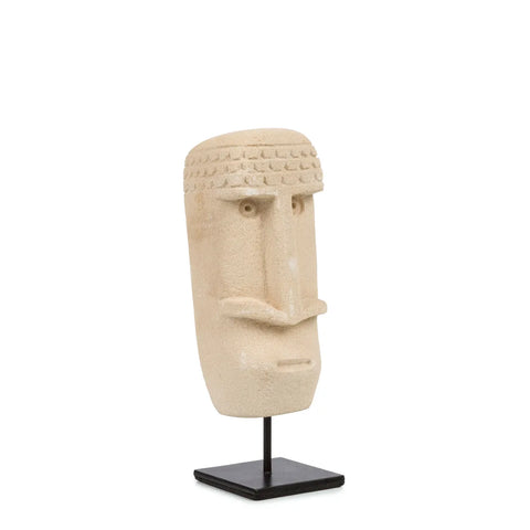 A beige, sculpted stone head with simple features and a textured hair pattern sits on a black metal stand. Hand carved from Sumba Stone, the art piece stands out against the plain white background, highlighting its minimalist design.