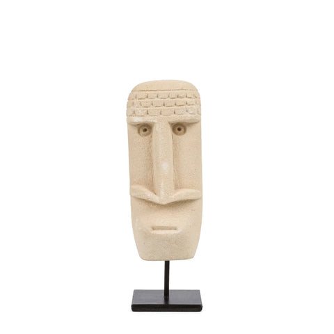 Hand-carved stone sculpture of a simplified human face with geometric features, including a rectangular nose and straight mouth, crafted from Sumba Stone. Set on a black stand against a white background, this piece captures timeless artistry in sandstone.