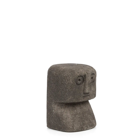 A small, abstract stone sculpture with a rectangular head and simplified facial features, including circular eyes and a straight mouth, resembles traditional Indonesian art. This piece recalls hand-carved sandstone Sumba stone statues, set against a plain white background.