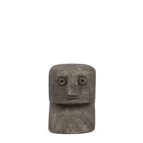 A small, abstract stone sculpture resembling a simplistic human face with large circular eyes and a straight-line mouth. The textured surface is reminiscent of traditional Indonesian art, giving the blocky, minimalist form an authentic hand-carved sandstone appeal.