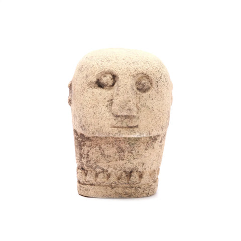 A small, hand-carved sandstone sculpture of a head with simple, abstract features, including round eyes and a flat nose. The surface is rough, with a beige hue and slight variations in texture, reminiscent of Sumba Stone craftsmanship.