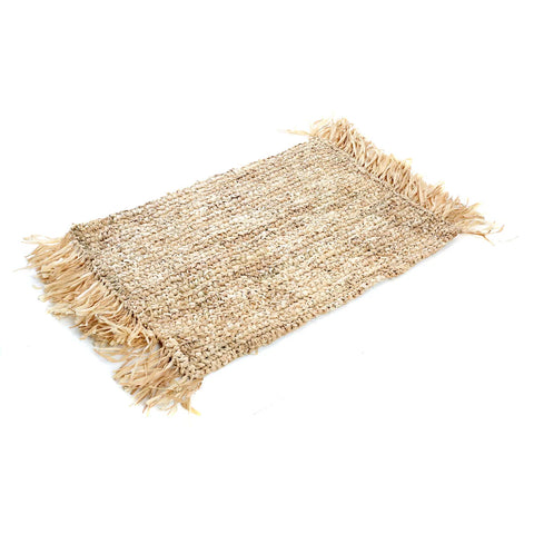 A rectangular, woven jute rug with fringed edges in a natural beige color is displayed on a white background. The coarse texture and rustic, handmade look add a boho touch to any space.