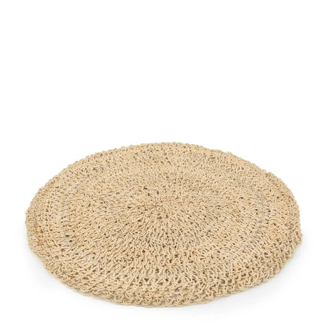 A round, woven, beige straw cushion laid flat on a white background evokes a natural table setting. Its texture appears handmade, featuring an intricate pattern of interwoven threads that add a boho touch.