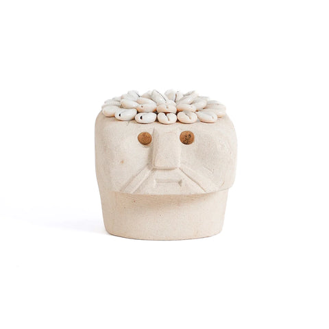 A beige ceramic sculpture with a simplified human face and a Sumba Stone aesthetic. The top is covered with small white stones, resembling hair. The facial features are minimal, with circular eyes and a straight mouth, giving it a hand-carved feel. The surface is smooth with a matte finish.