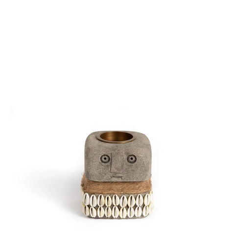 This cube-shaped, hand-carved candle holder elegantly displays a face design with circular eyes and a straight mouth. Adorned with cowrie shells and wrapped in twine, it serves as a unique tealight holder crafted from exquisite Sumba Stone.