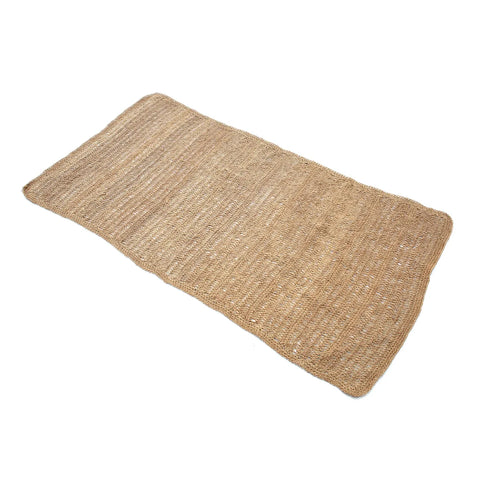 A rectangular woven jute rug with a natural, earthy color and simple design, similar to sisal. The textured fibers create a subtle striped pattern, and slightly curved edges suggest a handmade feel.