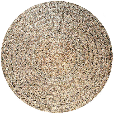 A large, round woven rug crafted from natural seagrass, featuring concentric circular patterns in soothing tones of beige and light brown. Its hardwearing texture is both coarse and elegant, making it a versatile choice for various interior styles.