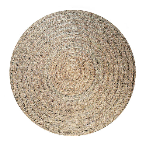 A round, woven jute rug with a natural color and a concentric circular pattern, reminiscent of raffia's rustic charm. The texture is visible, giving it an earthy and rustic appearance.