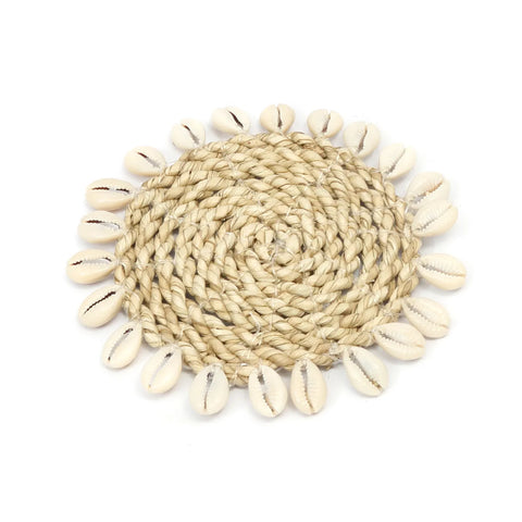 A circular woven mat made of light brown natural fibers, exuding an island style, bordered with white cowrie seashells.