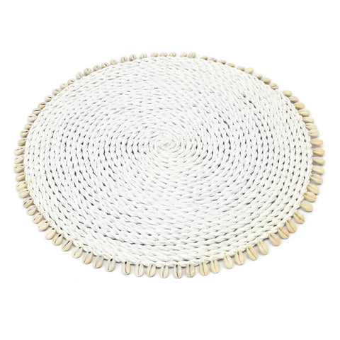 A round, woven white placemat with a braided texture and a border of small, beige cowrie seashells exudes a natural and rustic appearance. It's perfect for adding an island-style or bohemian touch to your table settings.