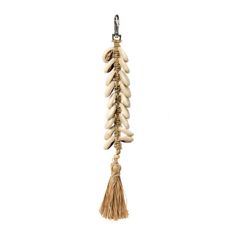 A decorative seashell keychain featuring cowrie shells woven into a vertical pattern on a beige cord, ending with a tassel of natural fibers that exudes boho luxury. The keychain includes a metal clasp at the top for easy attachment.