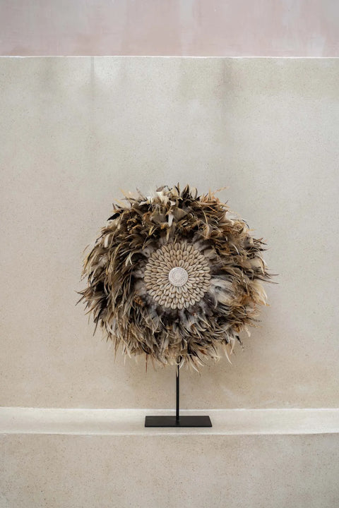 A bohemian beauty, this decorative wall piece showcases a circular arrangement of textured brown and beige feathers, centered around an intricate woven pattern. Perfect for a neutral background, this brown feather display adds an earthy charm to any space.