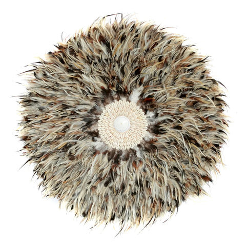 A circular Juju hat wall decoration made of soft feathers in shades of brown, cream, and black radiates from a textured central disk. This feather wall hung display adds bohemian beauty to any home interior with its fluffy and intricate pattern.