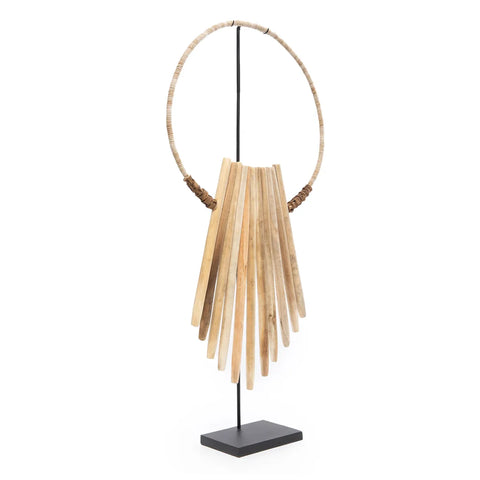 A decorative sculpture featuring a circular wicker frame with multiple elongated wooden slats, reminiscent of driftwood art, hanging in a staggered arrangement. This unique centerpiece is mounted vertically on a black metal stand with a rectangular base.