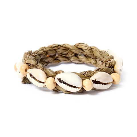 A braided bracelet made of natural fibers adorned with cowrie shells and small wooden beads. The earthy tones give it a bohemian look, reminiscent of coastal seagrass sway.