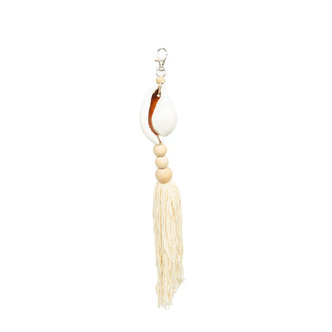 A seashell keychain featuring a large white shell and three wooden beads stacked vertically exudes Boho luxury. Below the beads, beige cotton tassels dangle, enhancing its bohemian style. The silver keychain hook stands out against the plain white background.