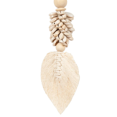 This handmade decorative piece exudes a bohemian atmosphere with its cluster of light beige shells, adorned by a woven leaf-shaped element and a delicate tassel hanging below. Connected by wooden beads, it brings an artisanal touch to any space.