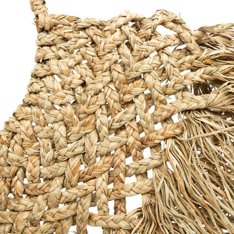 Close-up of an intricately woven straw or grass basket with coastal texture and detailed patterns, fringed edges adding an earthy boho vibe. The natural fibers form a textured and organic design, showcasing a mix of light and dark tones.