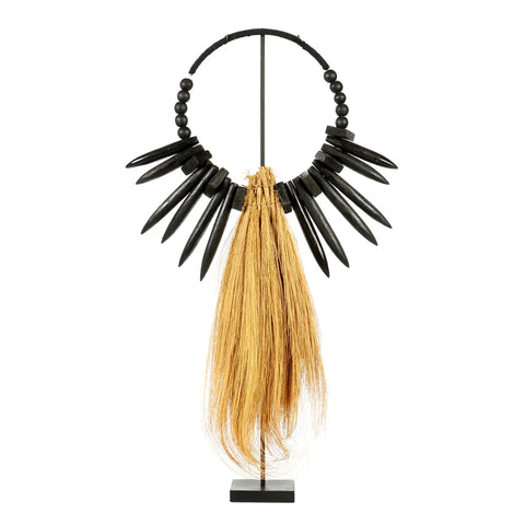 A decorative necklace displayed on a stand, featuring large black beads and pointed black spikes, exudes bohemian decor with its long, flowing light brown fibers of rayung grass hanging in the center, creating a striking contrast.