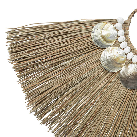 This alang grass display is a decorative piece crafted from dried fibers, arranged in a fan shape. Hand-placed shells, including large shiny seashells and smaller white ones, line the edge, exuding bohemian beauty with its natural, tropical aesthetic.