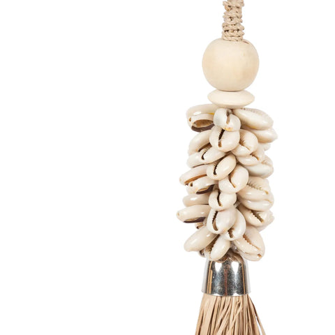 A decorative tassel exudes a bohemian atmosphere with its cluster of white cowrie shells and shiny metal cap, elegantly attached to a braided rope. A wooden bead sits above the shells, while natural fibers hang below, set against a plain white background.