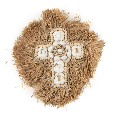 A decorative cross made of natural materials, featuring seashells and intricate beadwork, surrounded by a fringe of natural raffia. The design is textured and earthy, perfect for coastal decoration with a focus on organic elements.