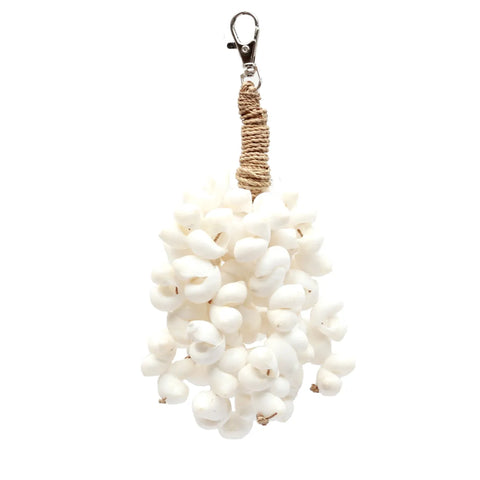 A cluster of small white shells is tightly bound with sea grass rope, forming a textured hanging ornament. Attached to a metal clasp at the top for easy display, this boho luxury piece shines against the plain white background, showcasing the natural beauty of its seashells.