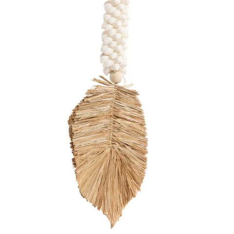 A decorative piece featuring a woven natural fiber leaf, reminiscent of bohemian atmosphere, hanging from a strand of white beads. The design is simple, with the leaf displaying a textured surface and a light brown color, contrasting against the smooth beads above it.