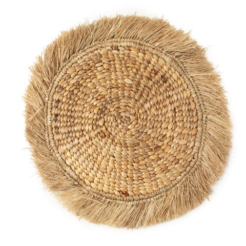 A round woven placemat made from natural fibers, featuring a braided center and fringe border. With its light brown and beige hues, it exudes a rustic, boho interior charm. Perfect as raffia placemats for adding an earthy touch to any dining setting.