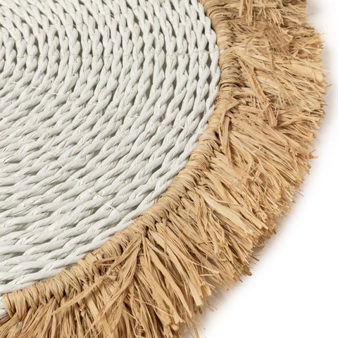 Close-up of a round woven seagrass placemat featuring a white braided center and fringed natural fibers, adding a textured, rustic charm perfect for a boho interior.