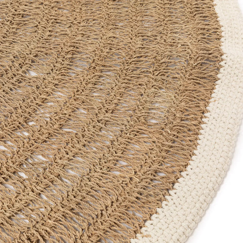 Close-up of a woven texture featuring braided crude fibers in a natural tone, bordered by a thick, cream-colored edge. The material, much like a seagrass carpet, is tightly woven, creating a patterned design on the surface that emphasizes its durability and style.