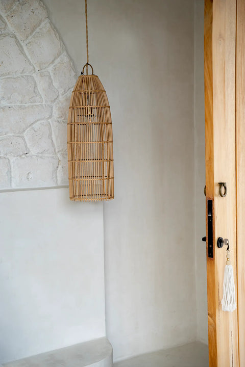 A minimalist living room exudes serenity with a rattan pendant light hanging beside a textured white wall. An open wooden door adorned with a white tassel enhances the natural ambiance, completing this tranquil setting with effortless charm.