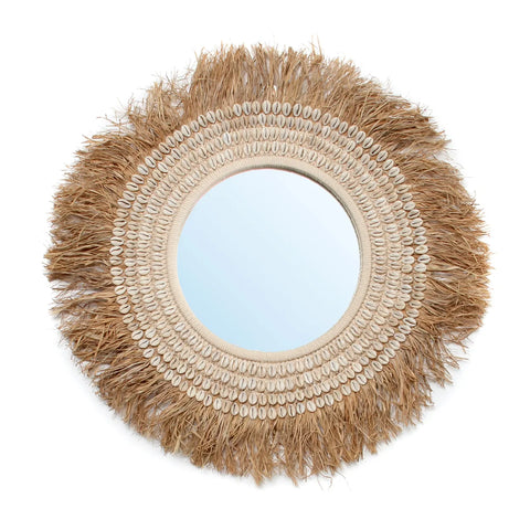 A round raffia mirror with a decorative frame made of straw and shells. The outer edge is fringed with straw, giving it a rustic, natural look perfect for bohemian decor. The central mirror reflects light, creating a bright focal point ideal for coastal home decor.