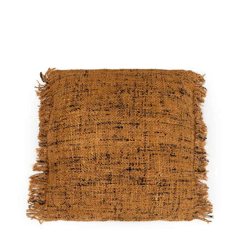 A square cotton cushion with a textured, woven fabric in a burnt orange color exudes a boho vibe. It features black speckles and fringed edges, creating a cozy, rustic appearance. The hand-dyed cushion is positioned against a plain white background.