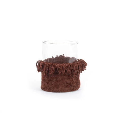 A clear Oh My Gee candle holder, wrapped in a textured, fringed brown fabric around the base like a cozy scarf, sits against a plain white background. Its design adds a touch of elegance reminiscent of velvet jackets.