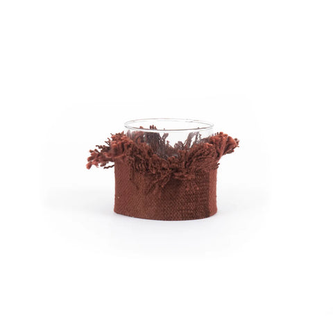 Hand-knitted charm embodies this glass candle holder, wrapped snugly in a textured, rust-colored fabric with fringe details at the top. Its design exudes warmth and coziness against a plain white background.