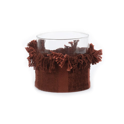 A clear glass jar with a decorative brown fringe wrapped around its lower half, featuring tassels that add texture and style, serves as a charming candle holder. The jar's contrast with the soft, velvet-like material creates a cozy, artisanal look that enhances any colour theme.