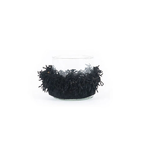 A clear glass container adorned with a textured, black fringe around its middle adds a touch of sophistication to any home decor. The dense, looped fibers give the vase a decorative and unique appearance against a white background, much like the luxe texture of velvet jackets.